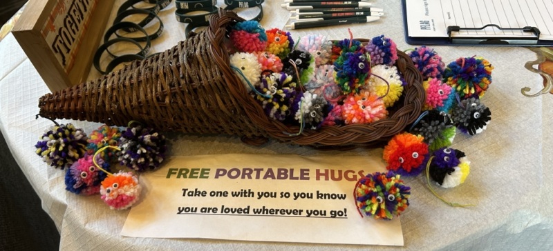Cornicopia filled with yarn crafted portable hugs with a sign "Free Portable Hugs Take one with you so you know you are loved wherever you go!"