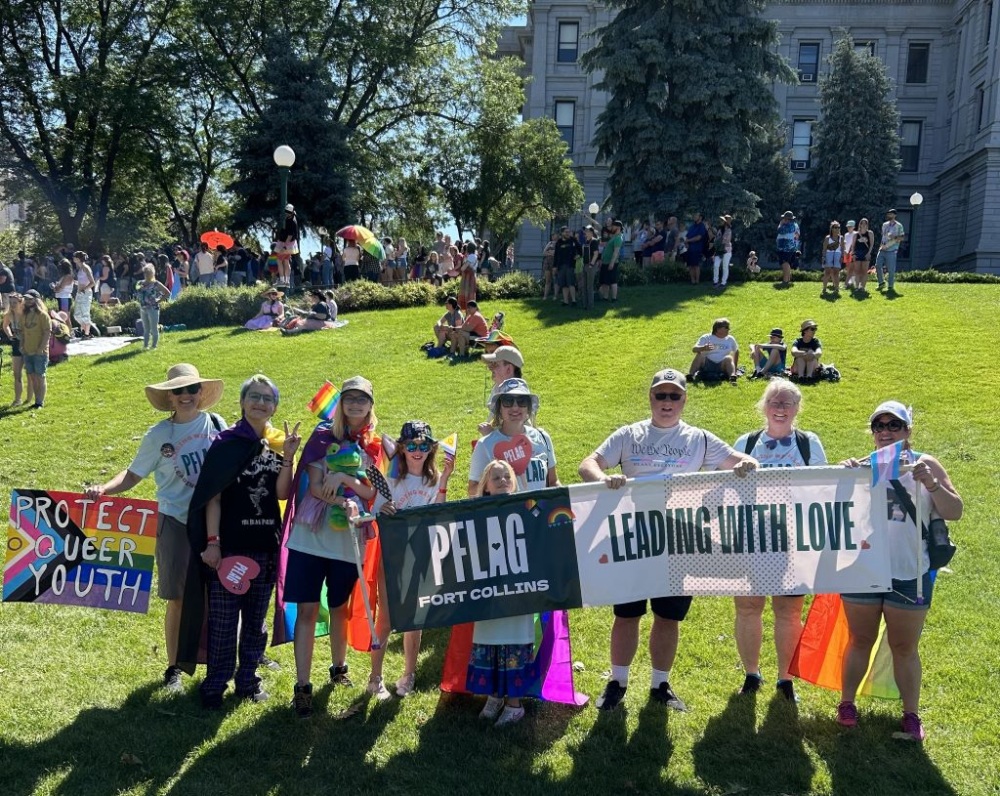 Group of wonderful volunteers, board members and allies holding a large PFLAG Fort Collins banner at Denver Pride, 2023