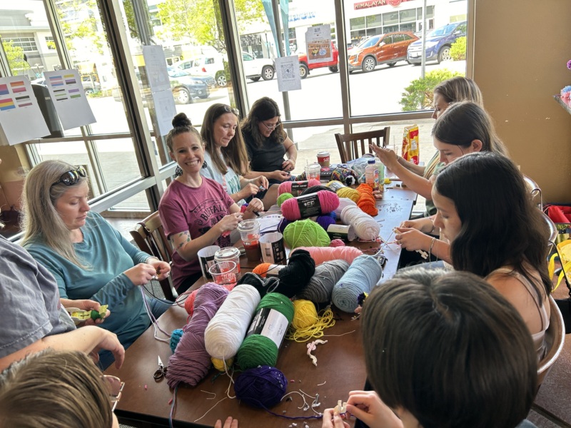 A group of PFLAG Fort Collins' wonderful volunteers making some amazing portable hugs(pom poms with googly eyes) in a café.