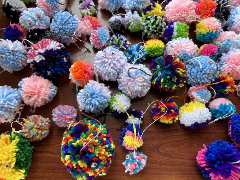 A pile of our beautiful pride colored portable hugs(pom poms with googly eyes), handmade by our wonderful volunteers.