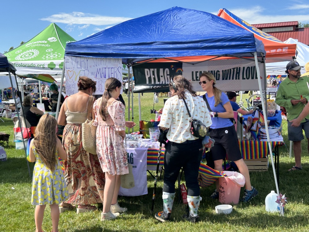 A group of people gather around a PFLAG booth at a Pride event.